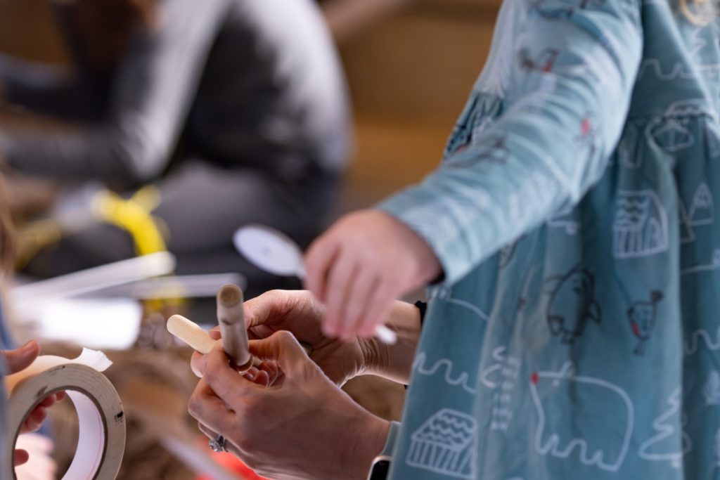 People work with tape and small wooden tools at a table