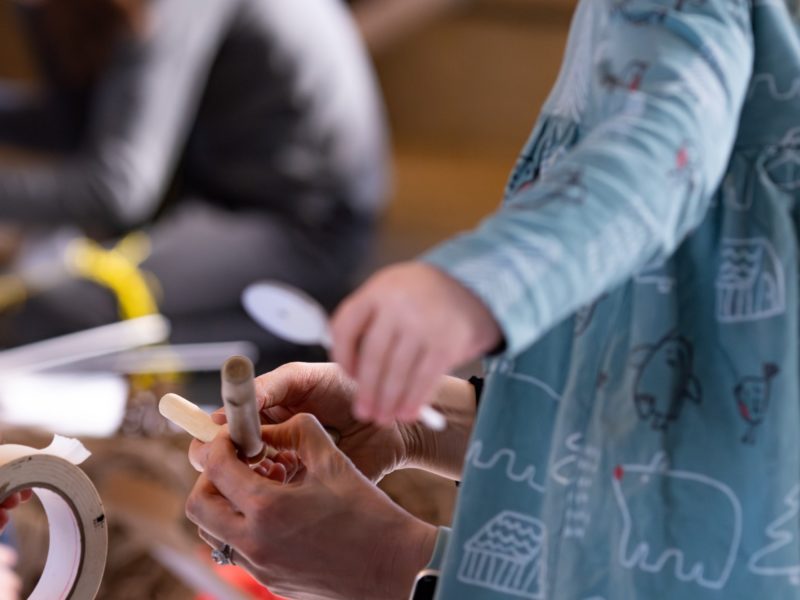 People work with tape and small wooden tools at a table