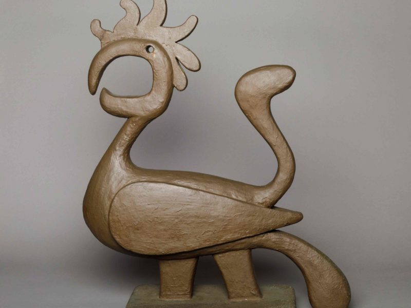 Tan abstract sculpture of a seated, horned animal-like figure with curved limbs on a rectangular base